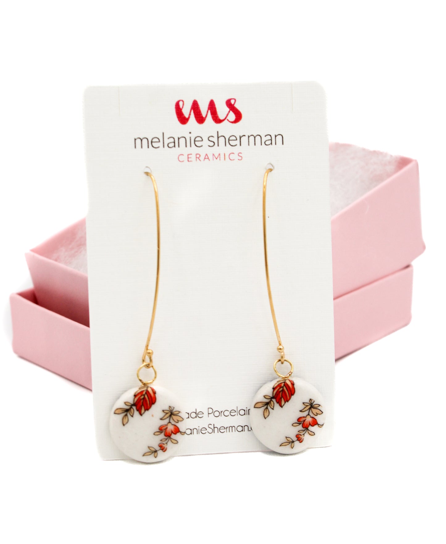 Gold-filled round porcelain dangle earrings with vintage orange flower designs are displayed against a card labeled Melanie Sherman Ceramics, beautifully nestled in a pink box. Product Name: Porcelain Dangle Earrings Orange 2 Flowers.