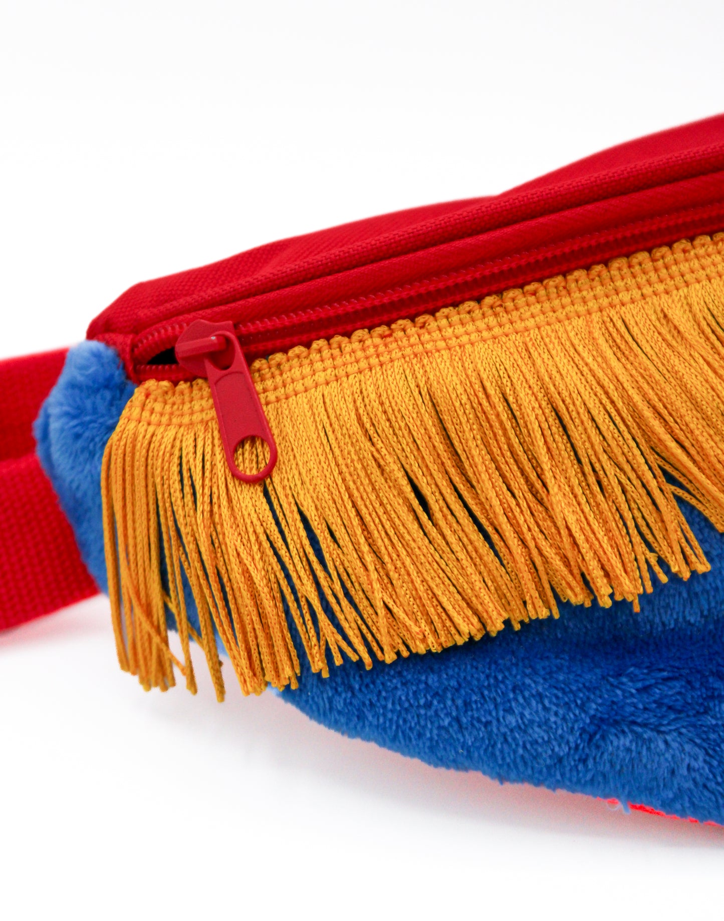 Close-up of the Fringe Fanny Pack - Yellow, featuring a blue plush faux fur exterior, red zipper and strap, and yellow fringes, creating a vibrant waist accessory.