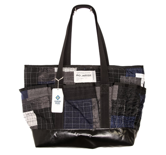 large, black and grey, tote bag with textured fabrics and a variety of stitching. Three pockets on front and mesh pocket on back with two top handle straps